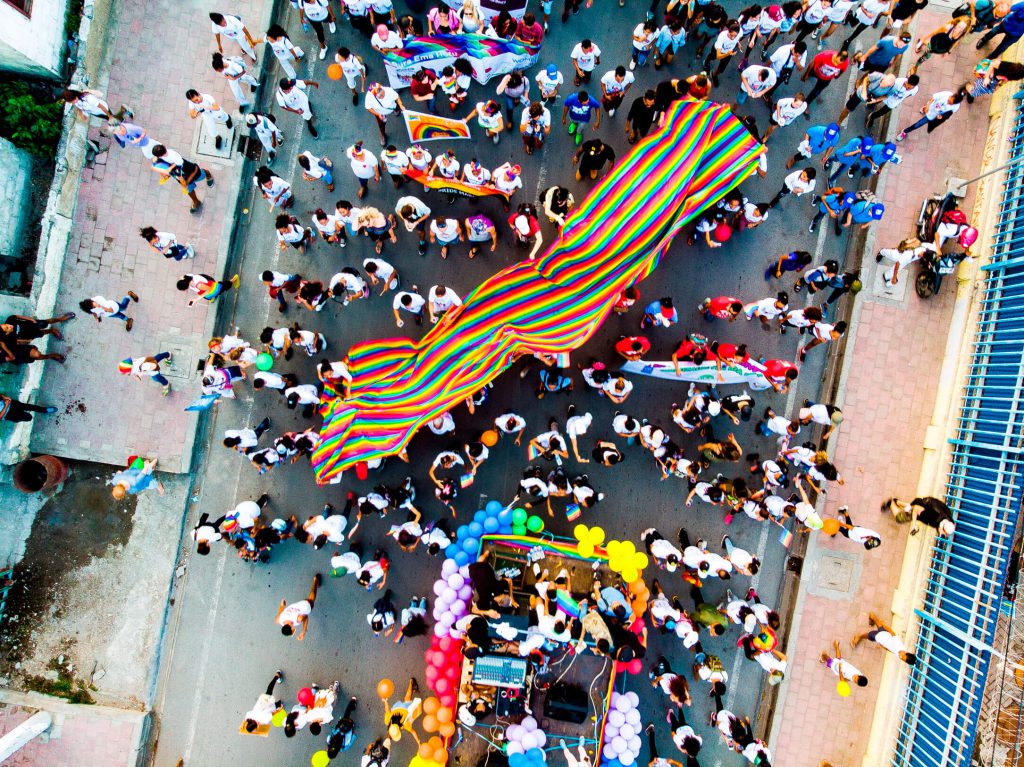 Drone shot of a street full of people holding the LGBTQIA+ flag during a Pride Parade.