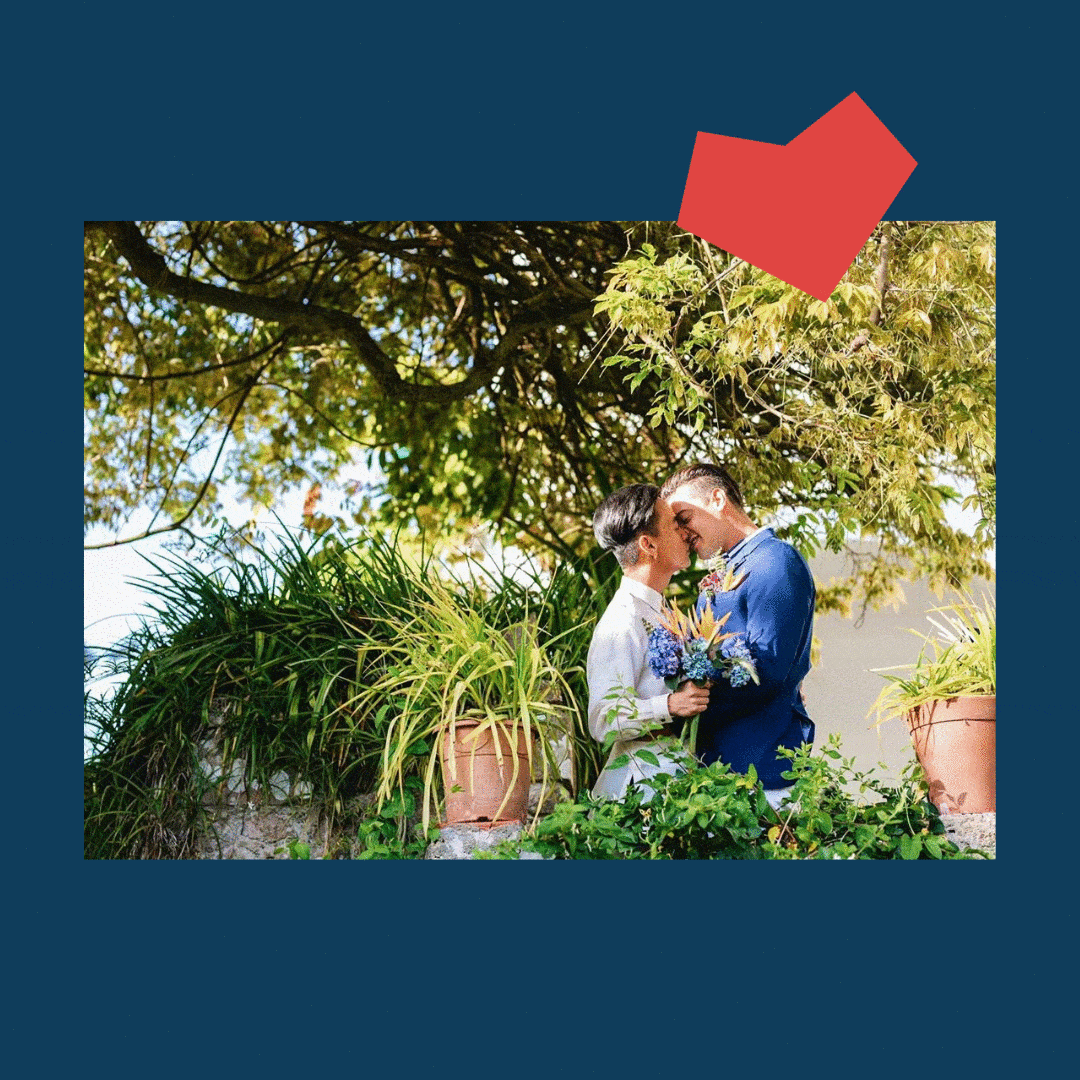 Couple of two men in a suit leaning in for a kiss in a place full of plants and trees.