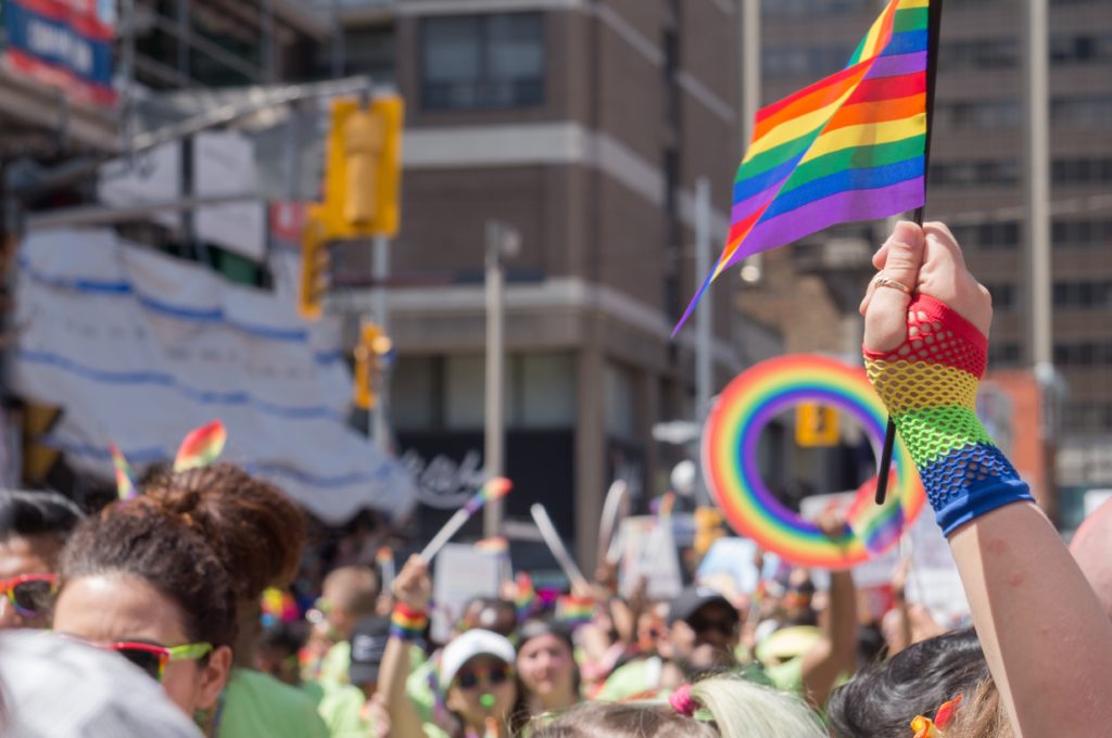 Hand wearing a rainbow glove, holding a LGBTQIA+ flag in a Pride Parade.