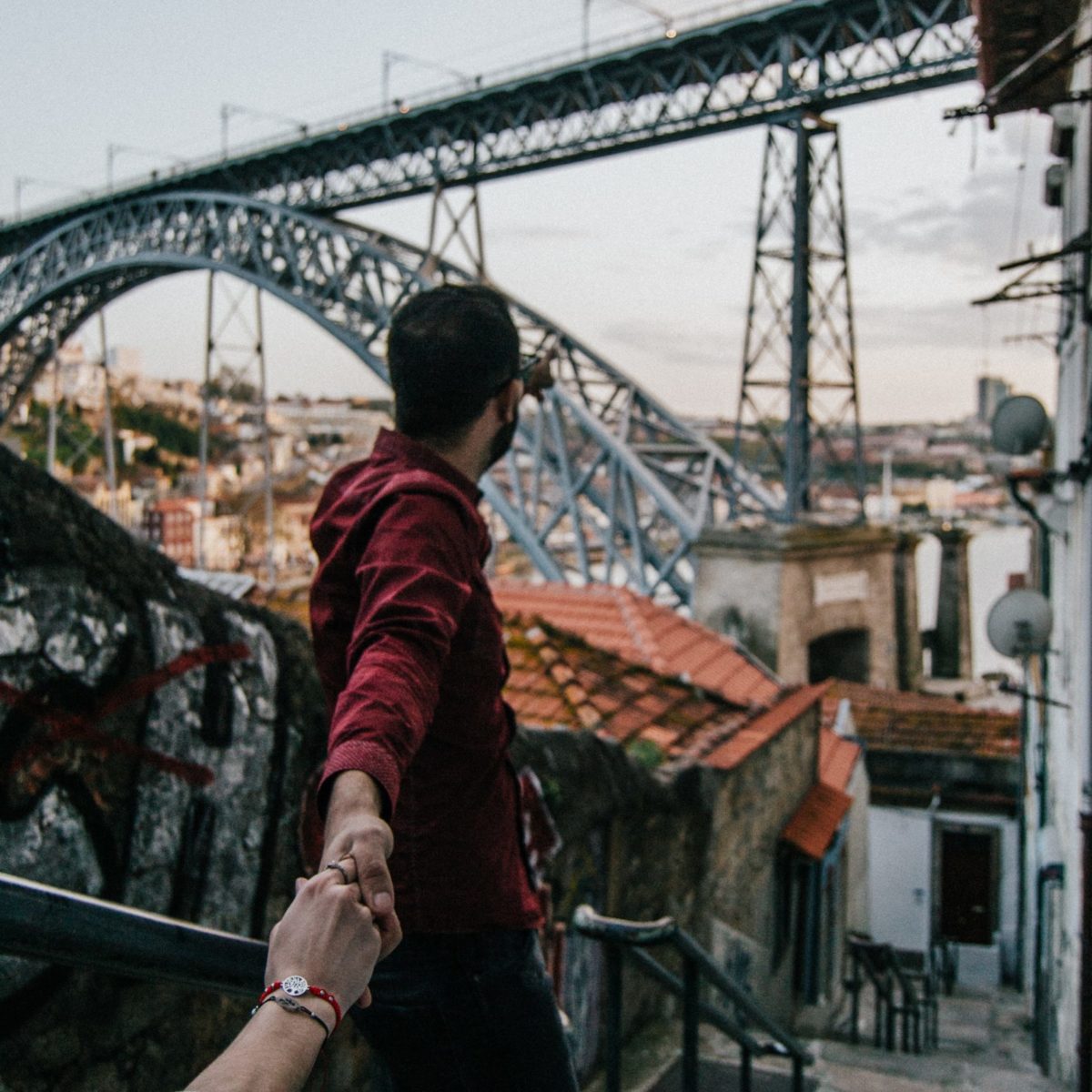 Couple in an alley in Porto holding hands. In the background there’s D. Luís I bridge.