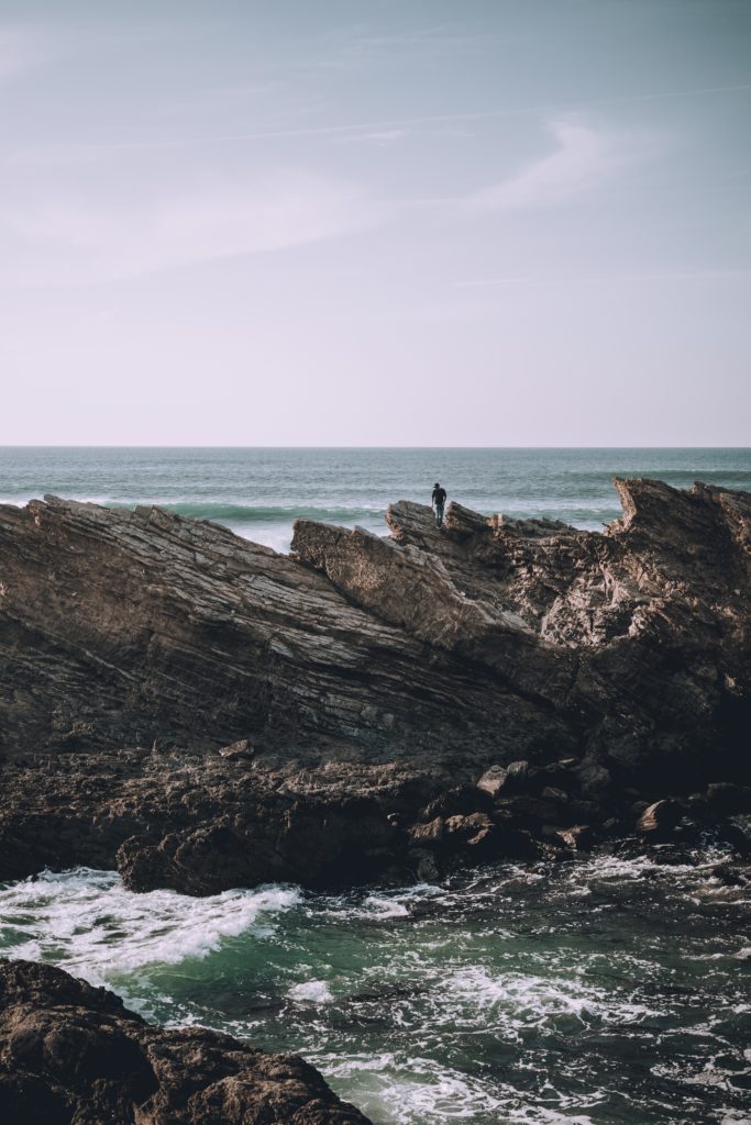 A person exploring on the rocks surrounded by the sea.