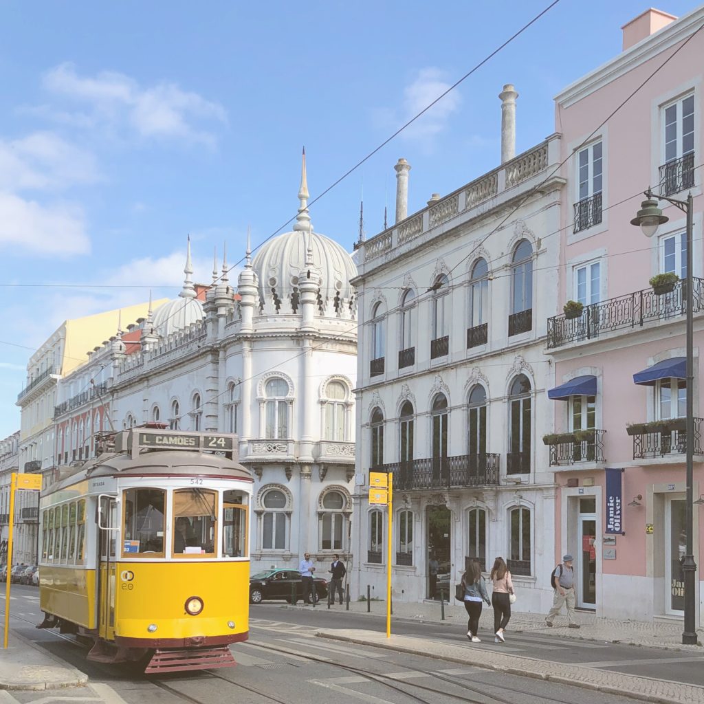 A yellow tram passing by some white buildings in Lisbon.