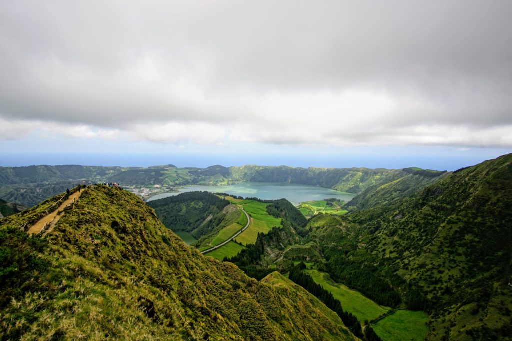 Sky-view of the lush green landscape in Azores Island, with a lake in the middle.